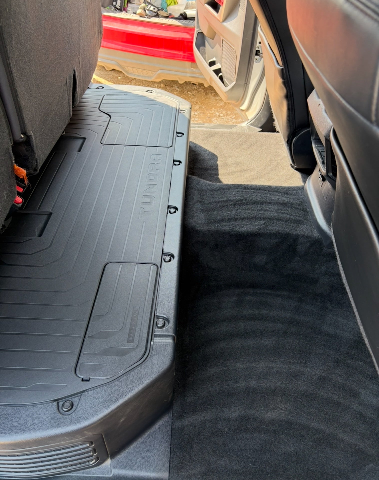 Car trunk with a black floor mat and open car door in the background.