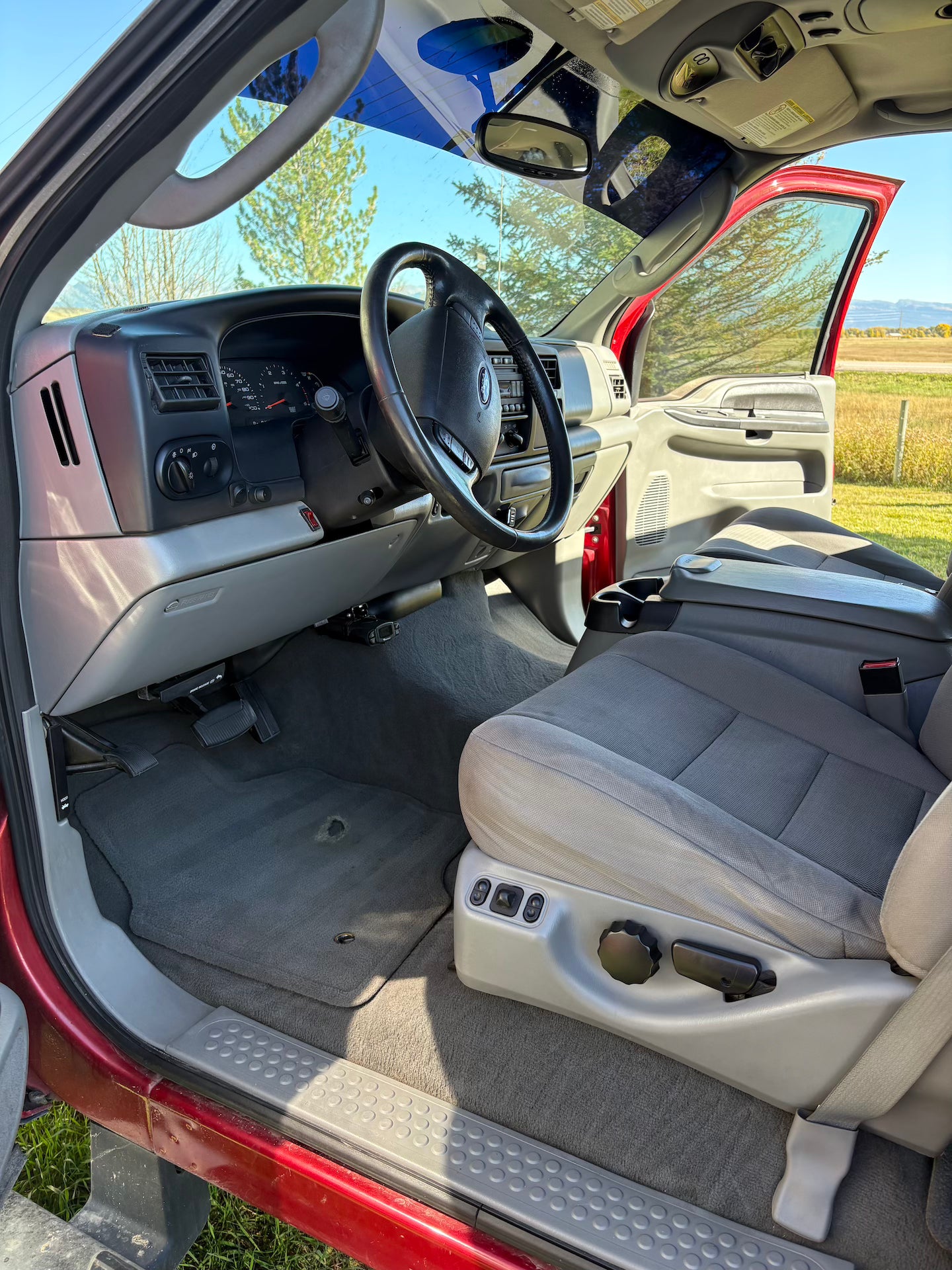 Interior of a red truck with gray seats and dashboard, open door showing grassy area outside.
