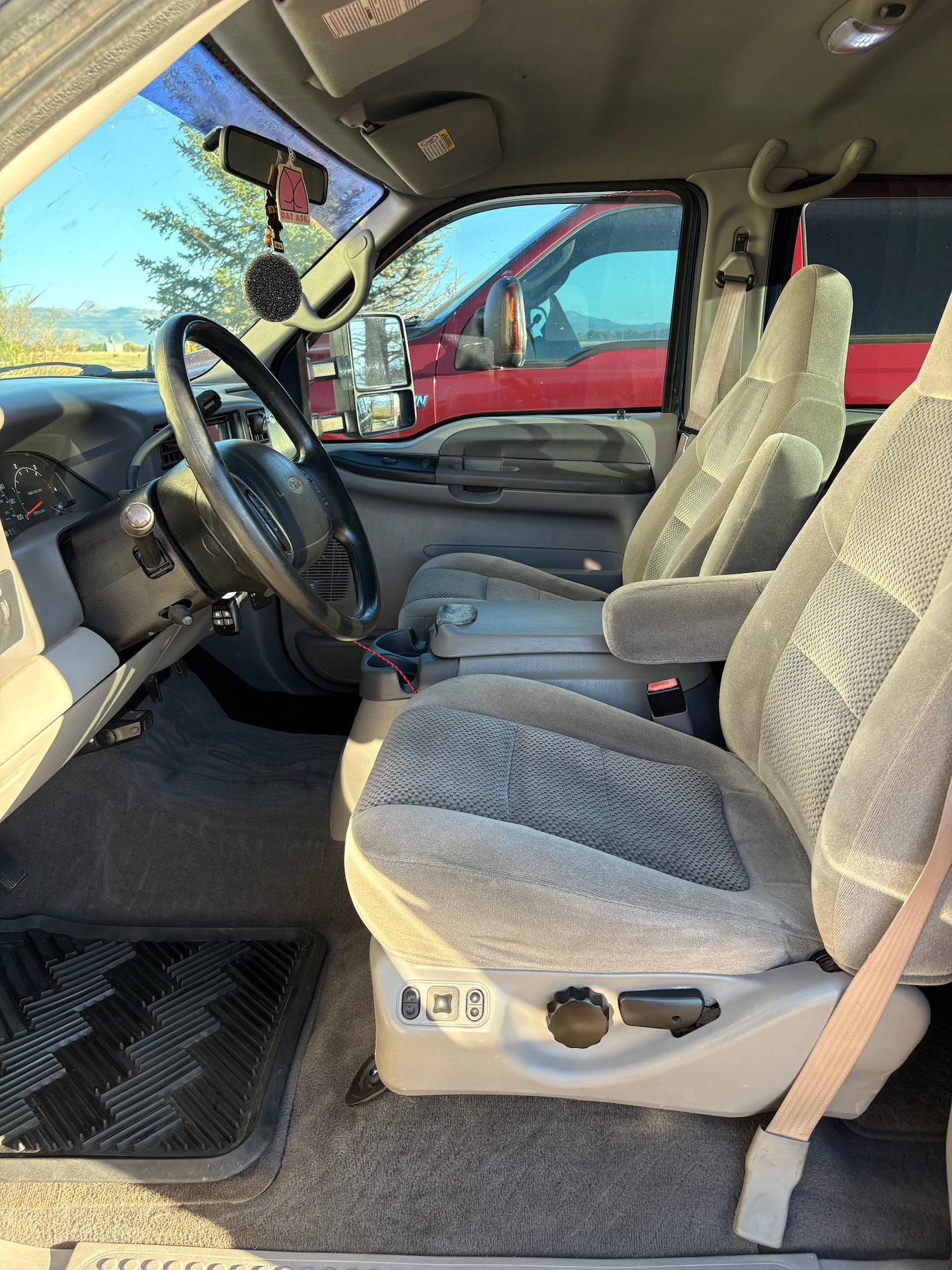 Interior of a vehicle with gray seats and dashboard, showing a clear sky outside.