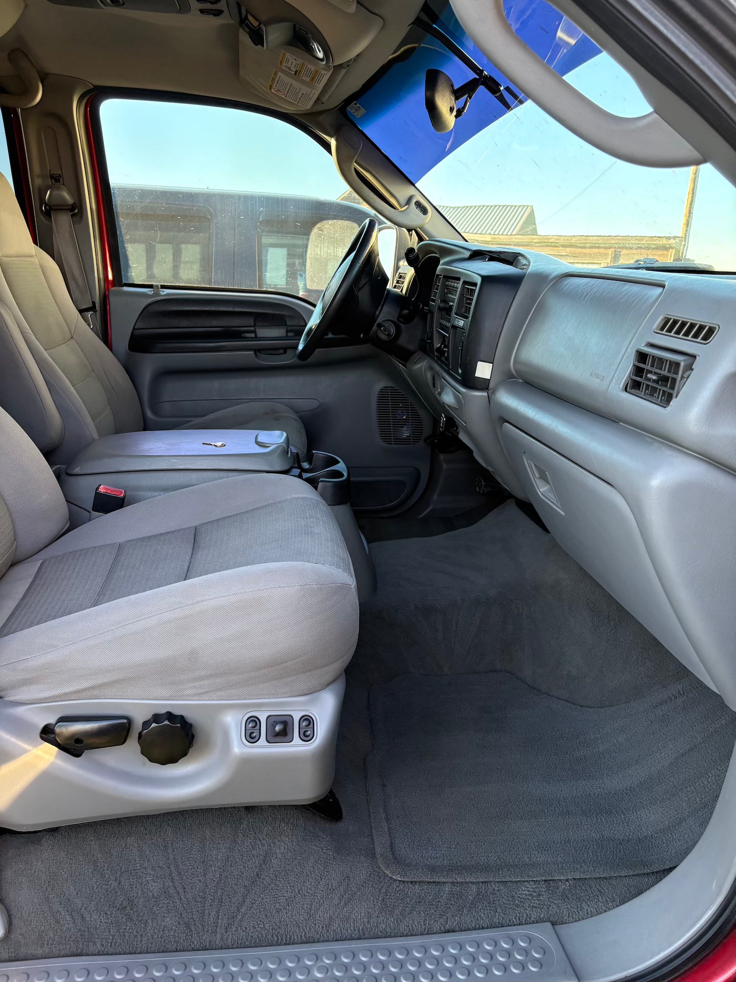 Interior of a vehicle with beige seats and dashboard, showing the steering wheel and dashboard controls.