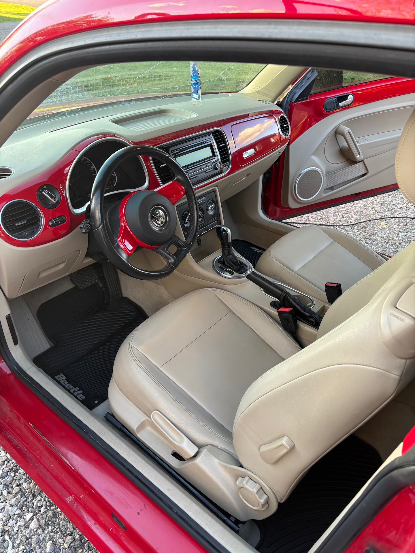 Car interior with red exterior, beige seats, and visible dashboard.