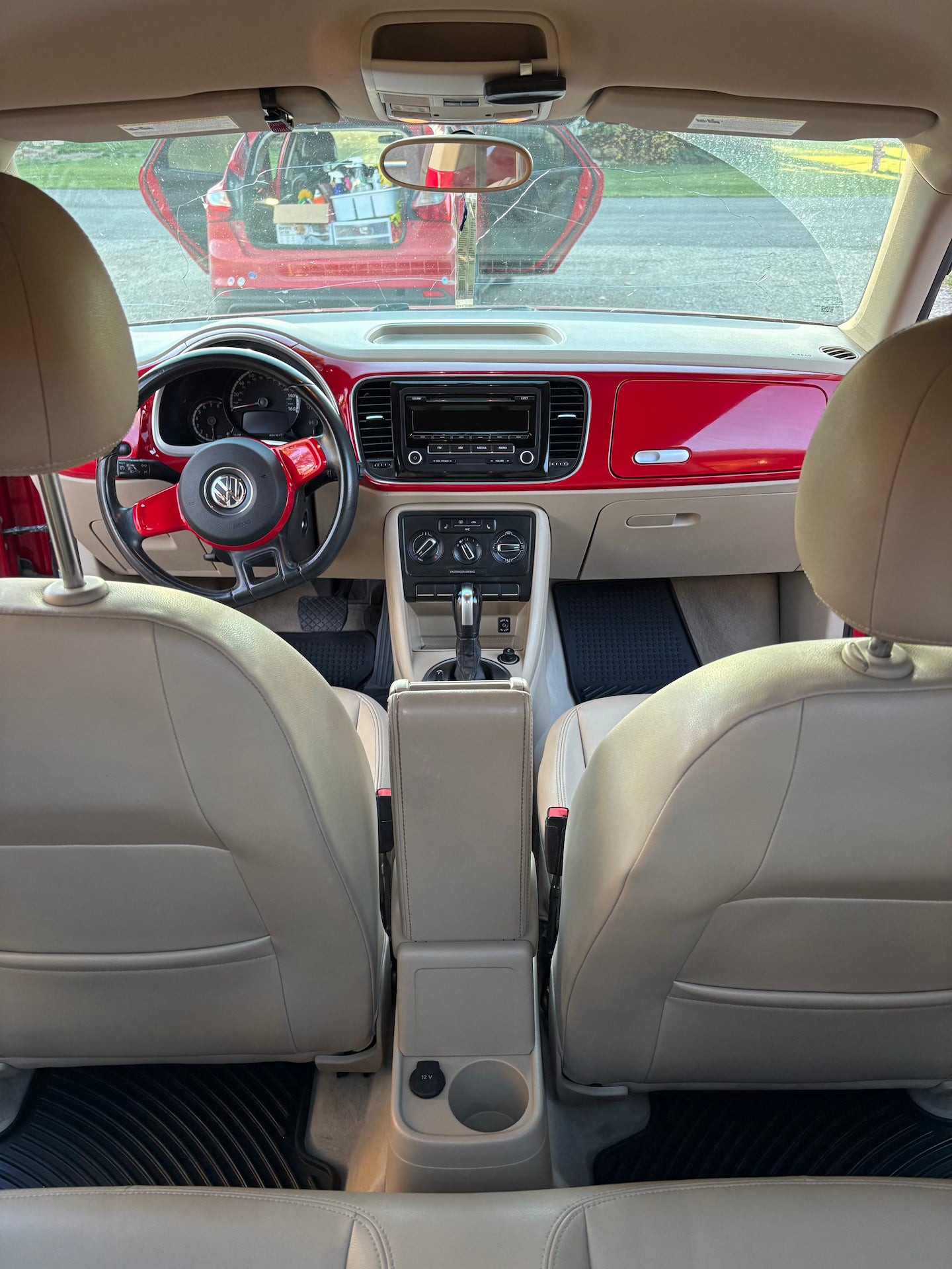 Car interior with beige seats and a red exterior visible through the windshield.