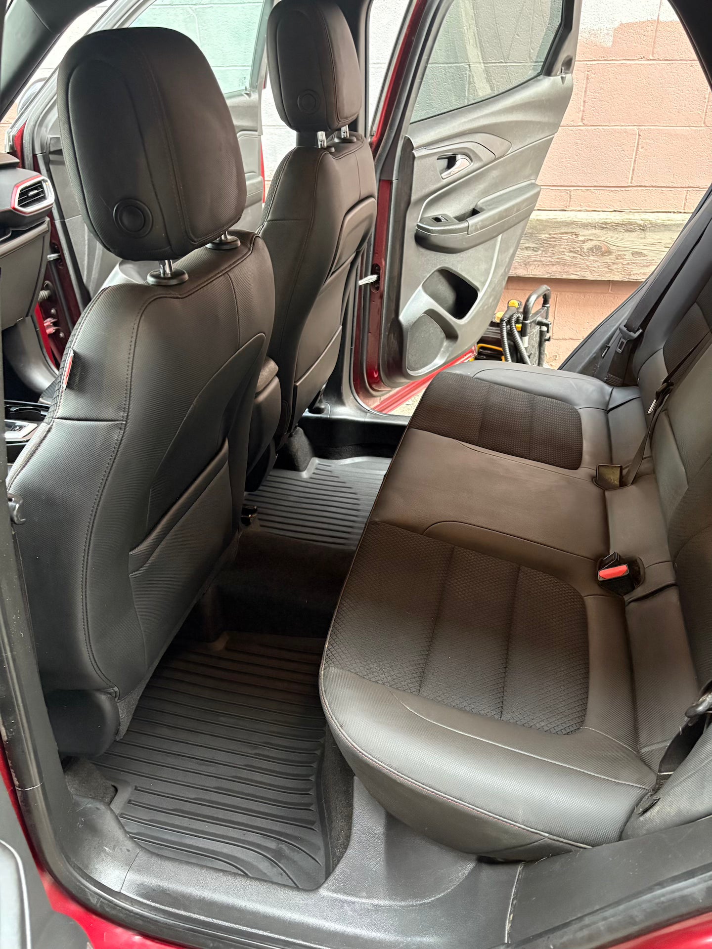 Car interior with brown leather seats and open door showing outdoor setting.