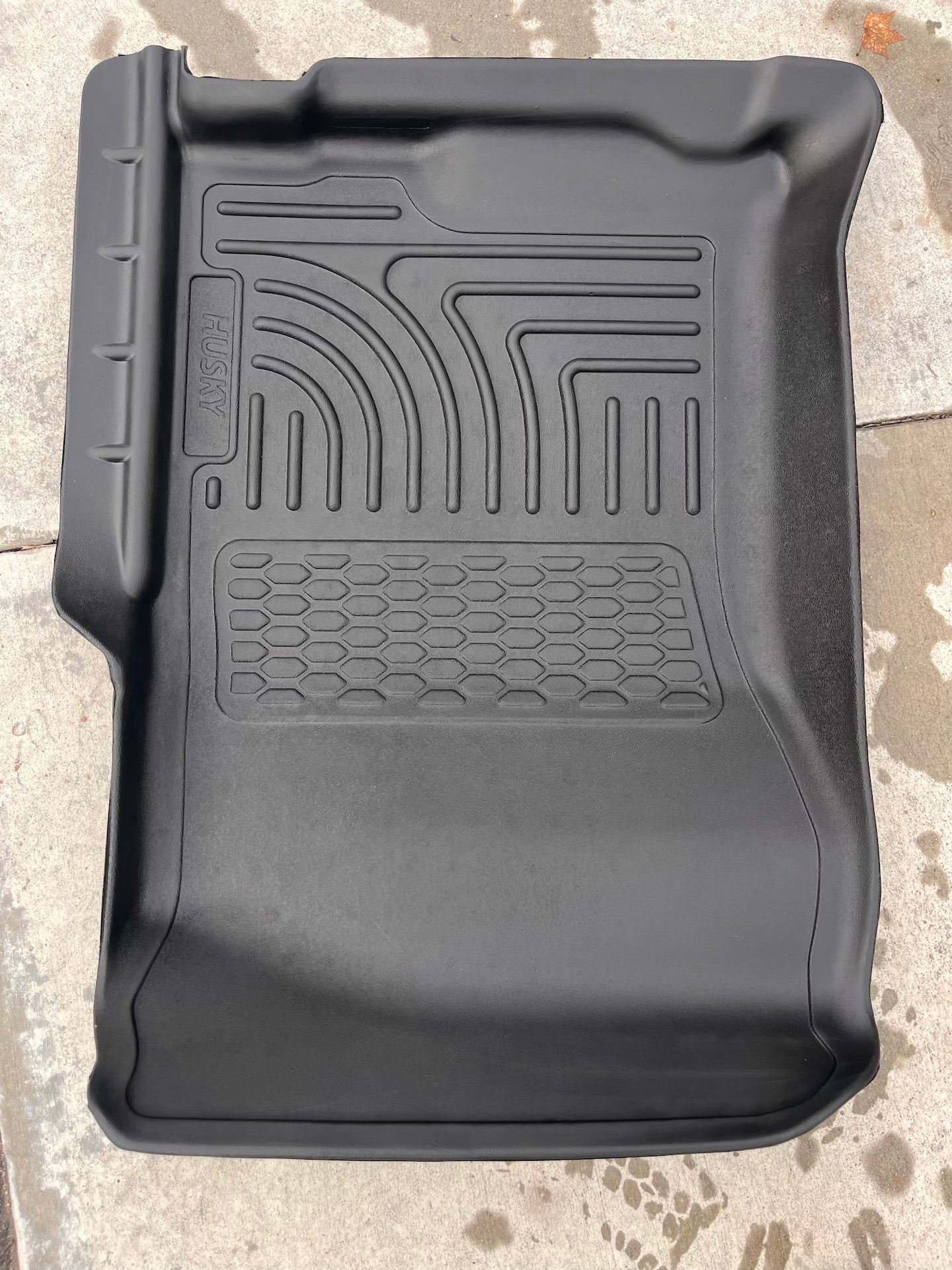Black car floor mat with textured pattern on a concrete surface